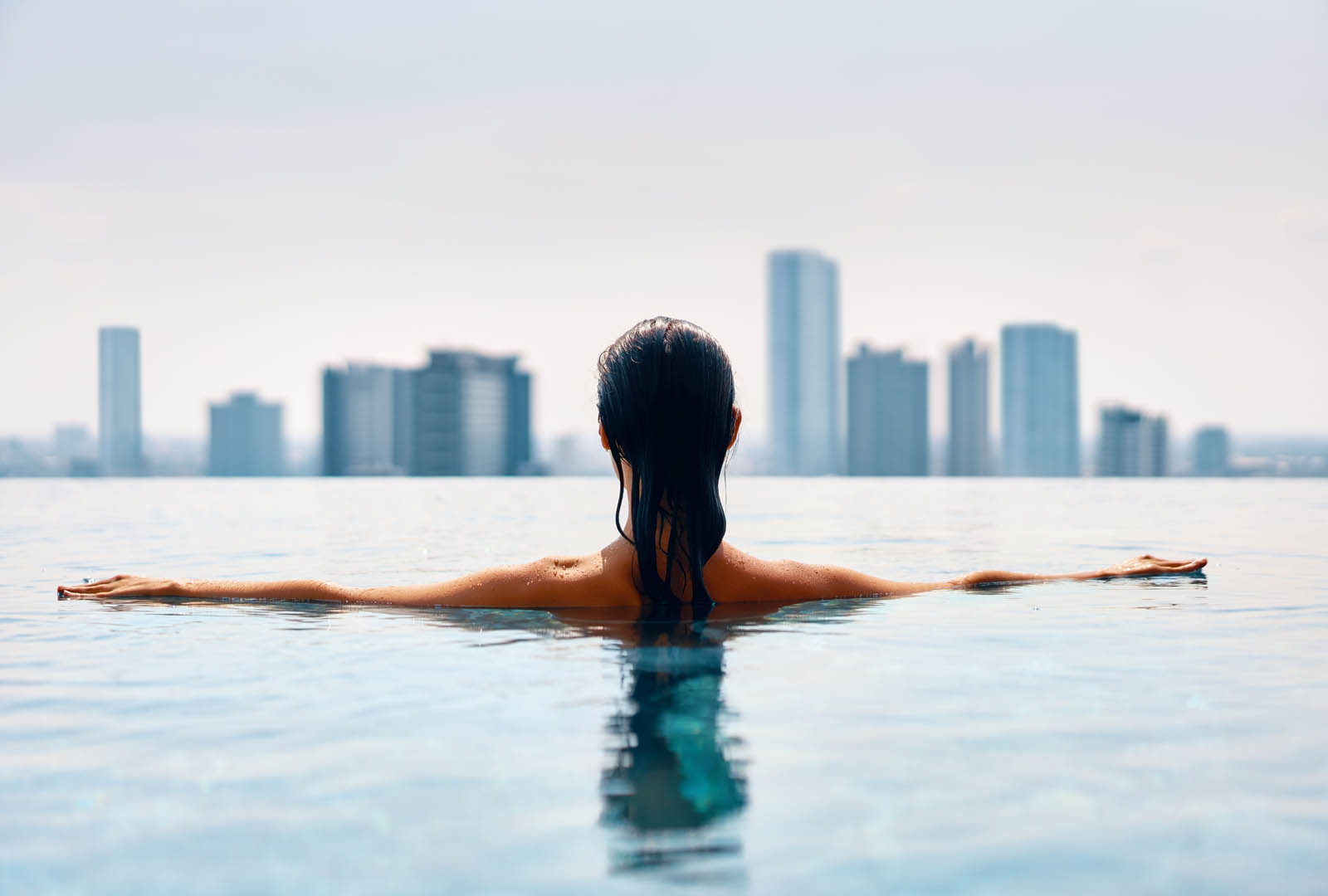 Back view of young woman swimming in swimming pool on roof top